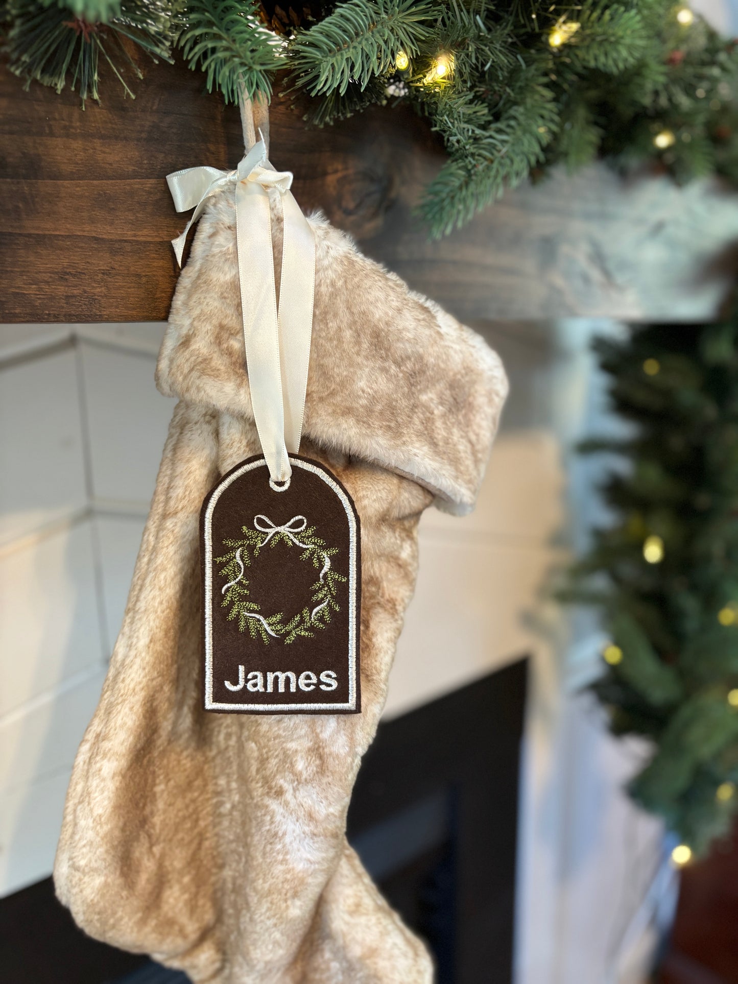 Beige Christmas stocking with 'James' tag hanging under a decorated tree.