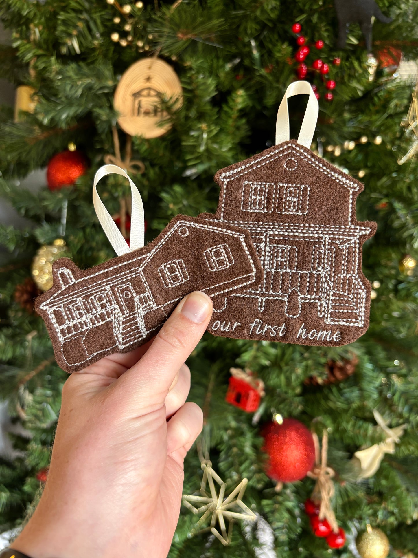 Decorative ornament shaped like a house held in front of a Christmas tree.