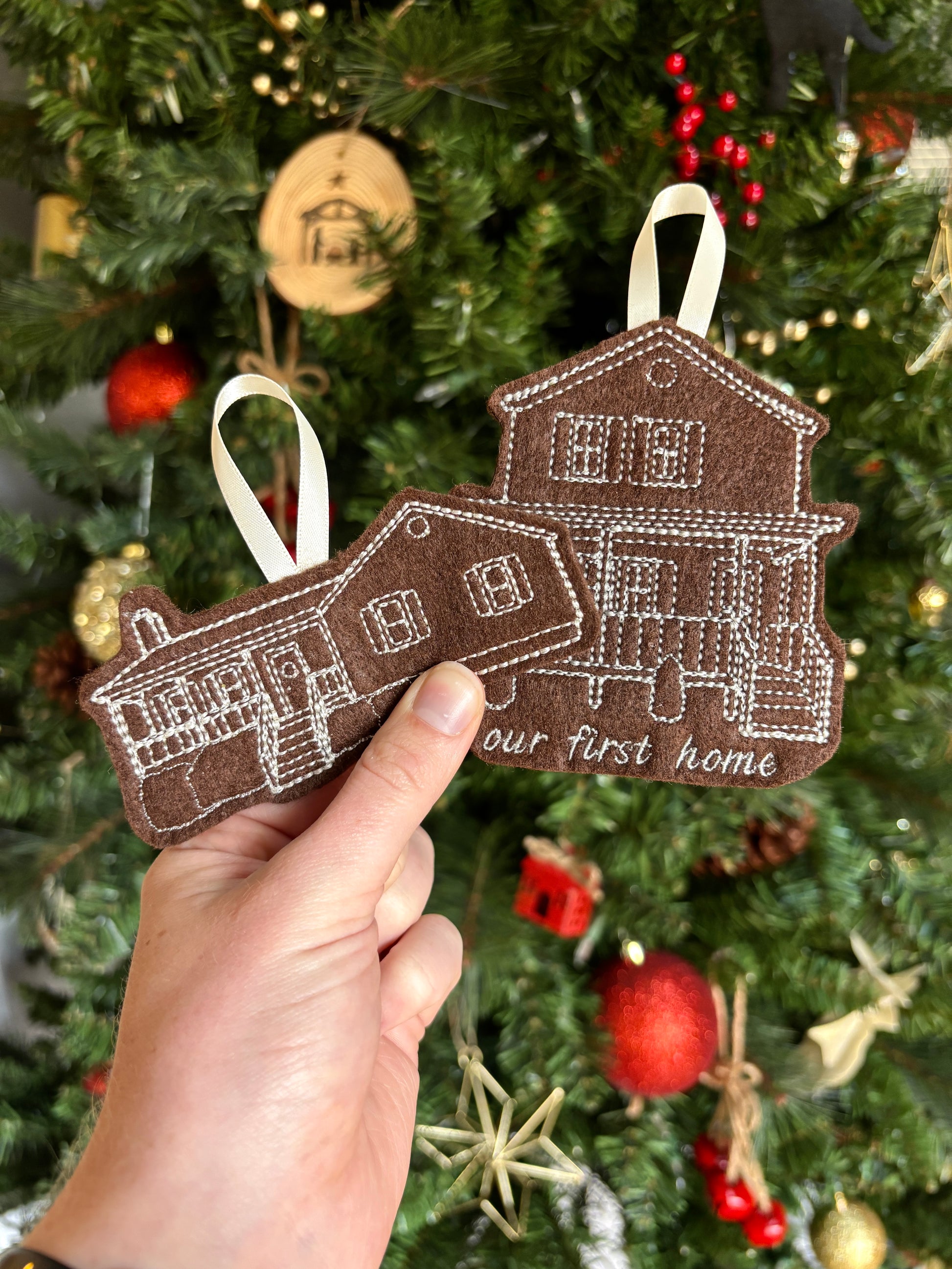 Decorative ornament shaped like a house held in front of a Christmas tree.