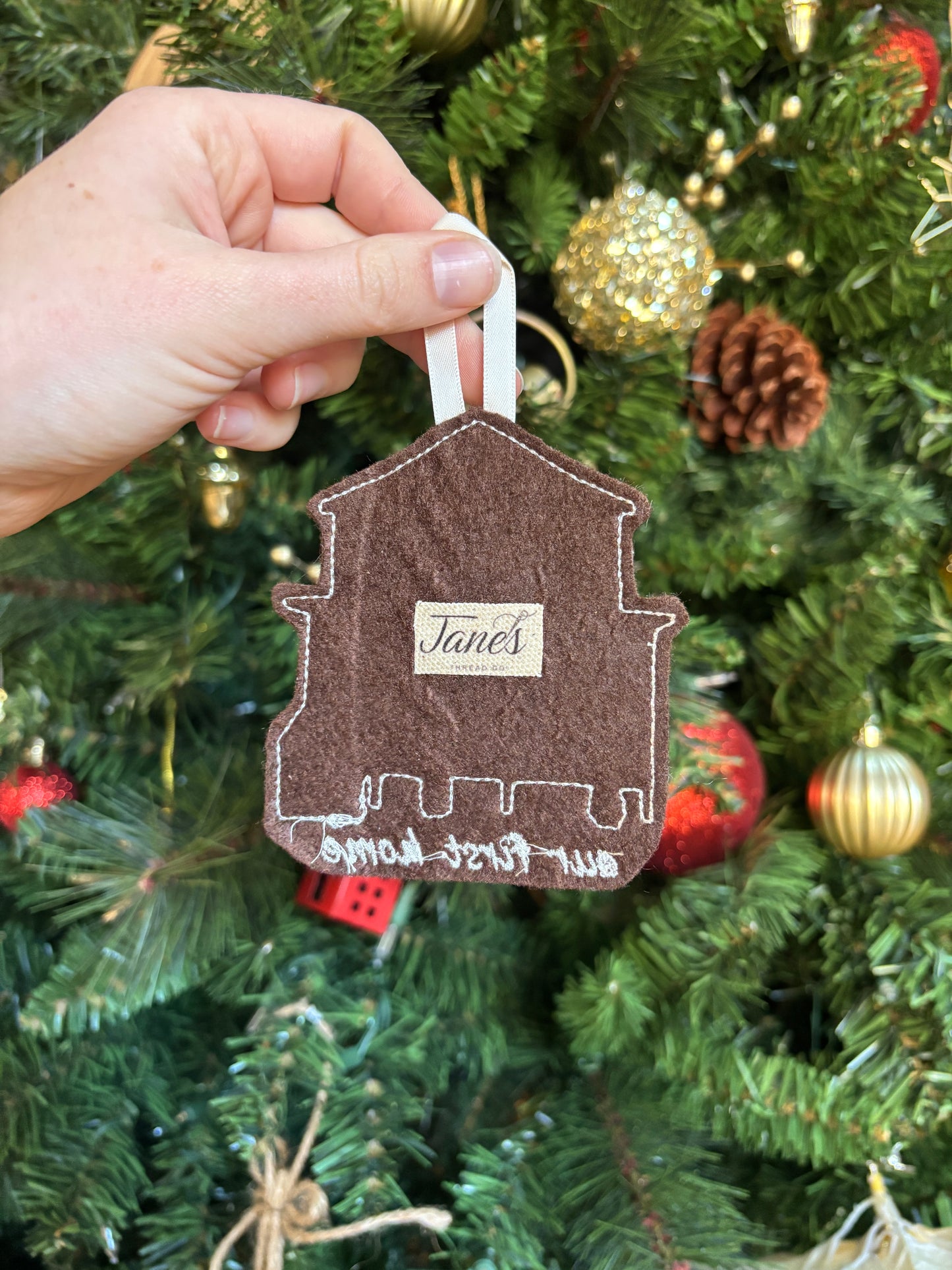Hand holding a decorative ornament shaped like a house against a Christmas tree background