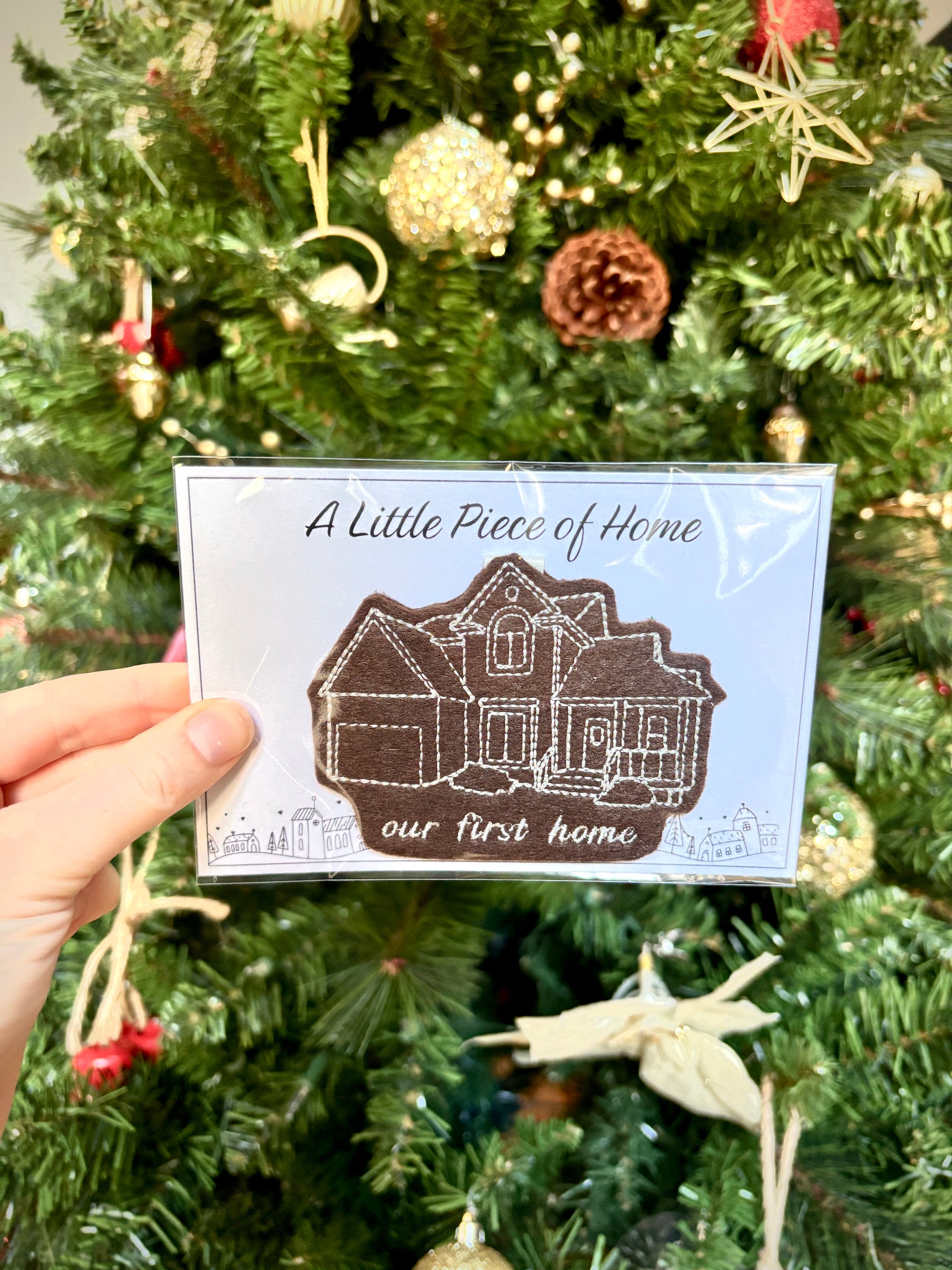 Card with house illustration held in front of a decorated Christmas tree