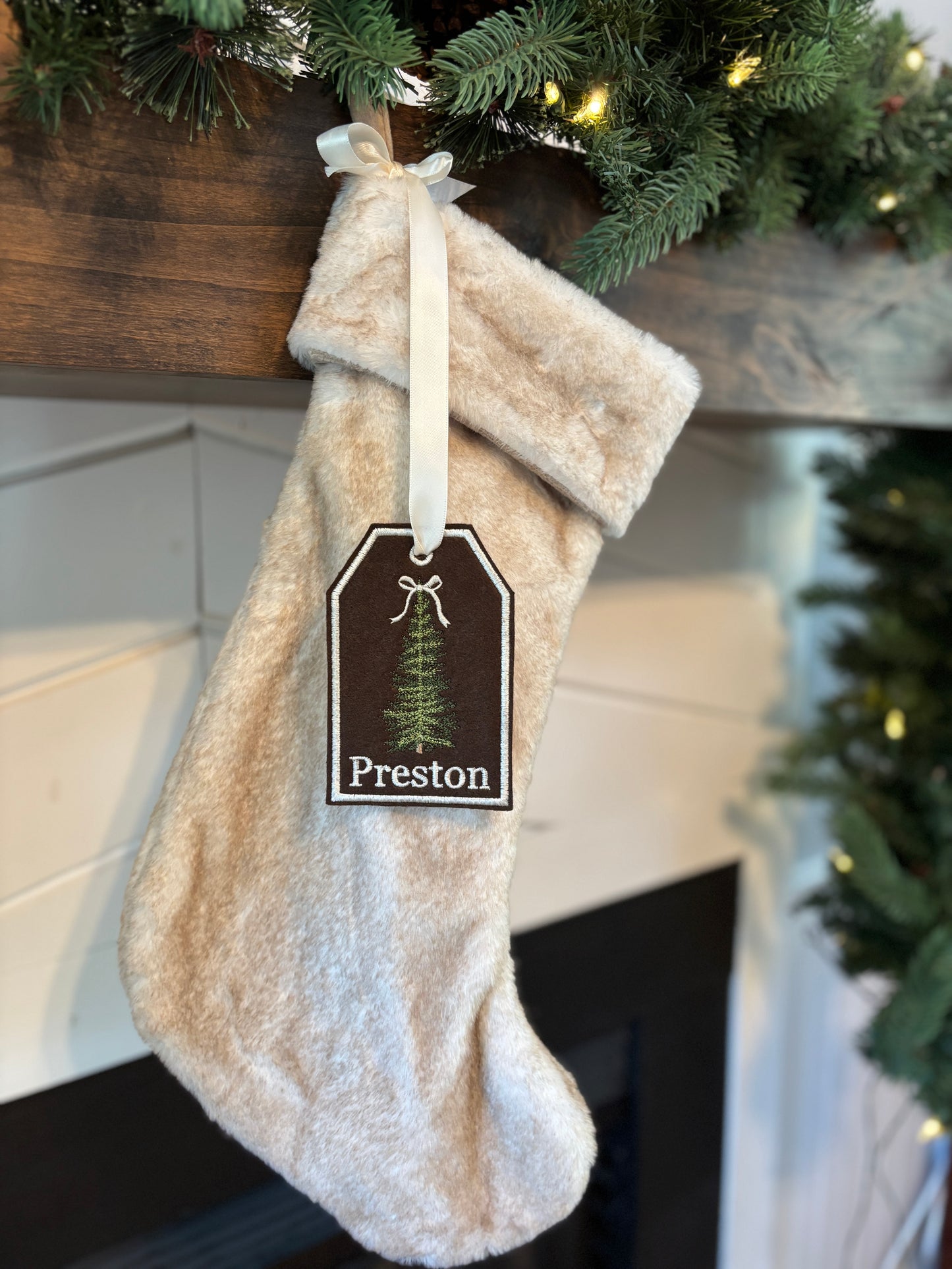 Beige Christmas stocking with a tag labeled 'Preston' hanging on a fireplace mantel.