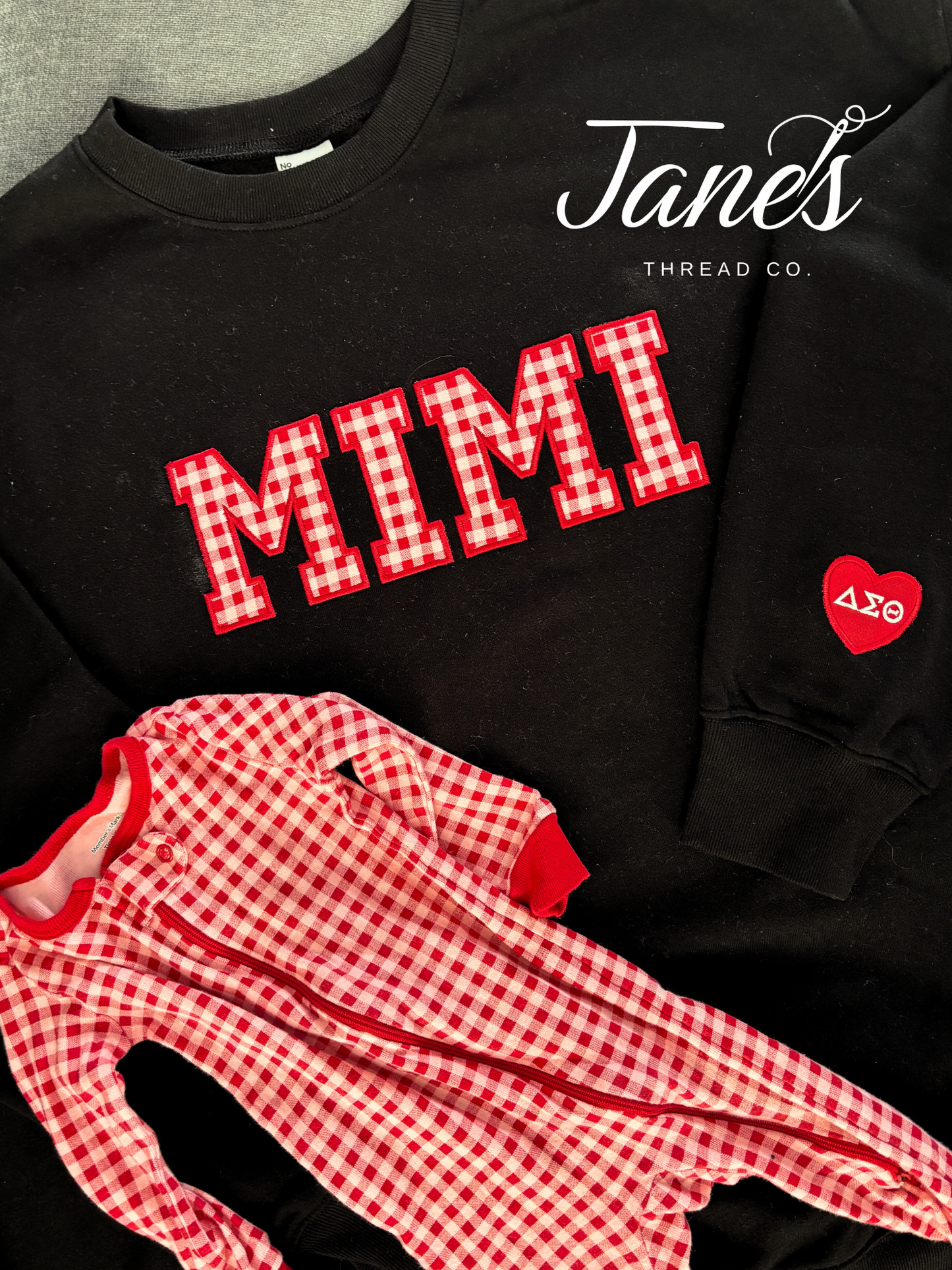 Black sweatshirt with 'MIMI' in red checkered letters and a matching red checkered outfit on a gray surface.
